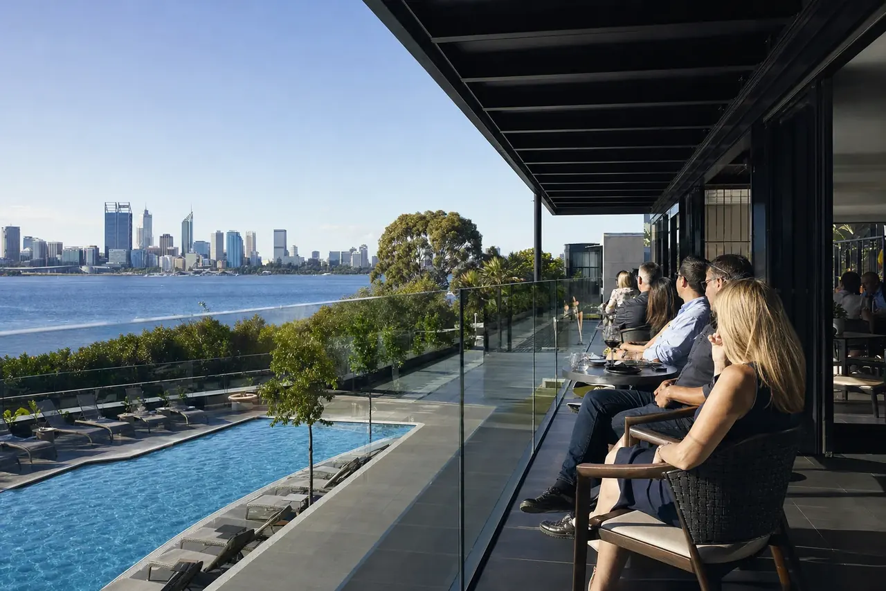 Guests on a Perth hotel terrace behind a frameless glass fence looking out over the pool at dusk